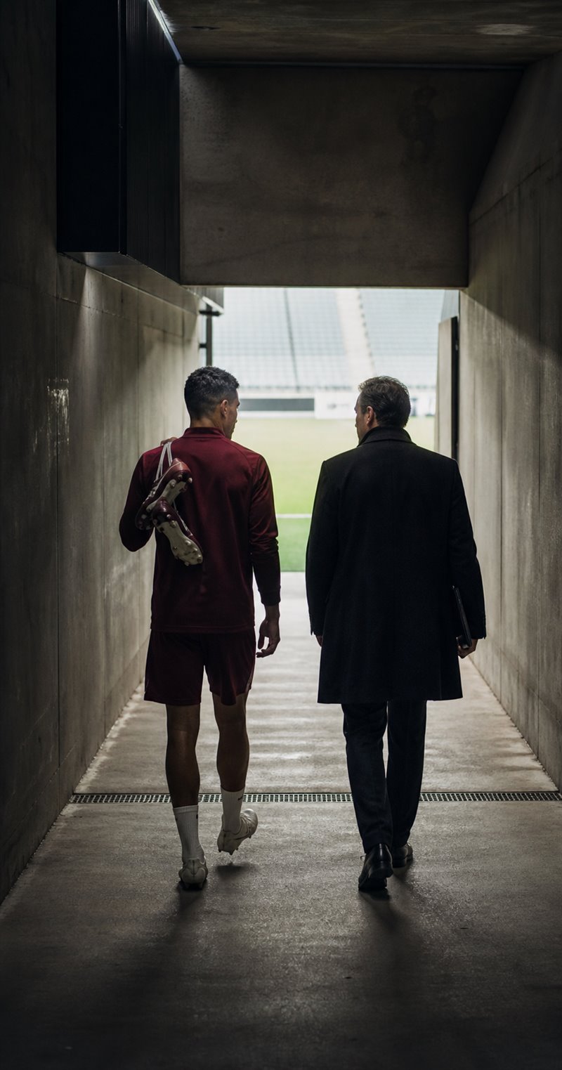 A footballer and his advisor walking together through a stadium tunnel